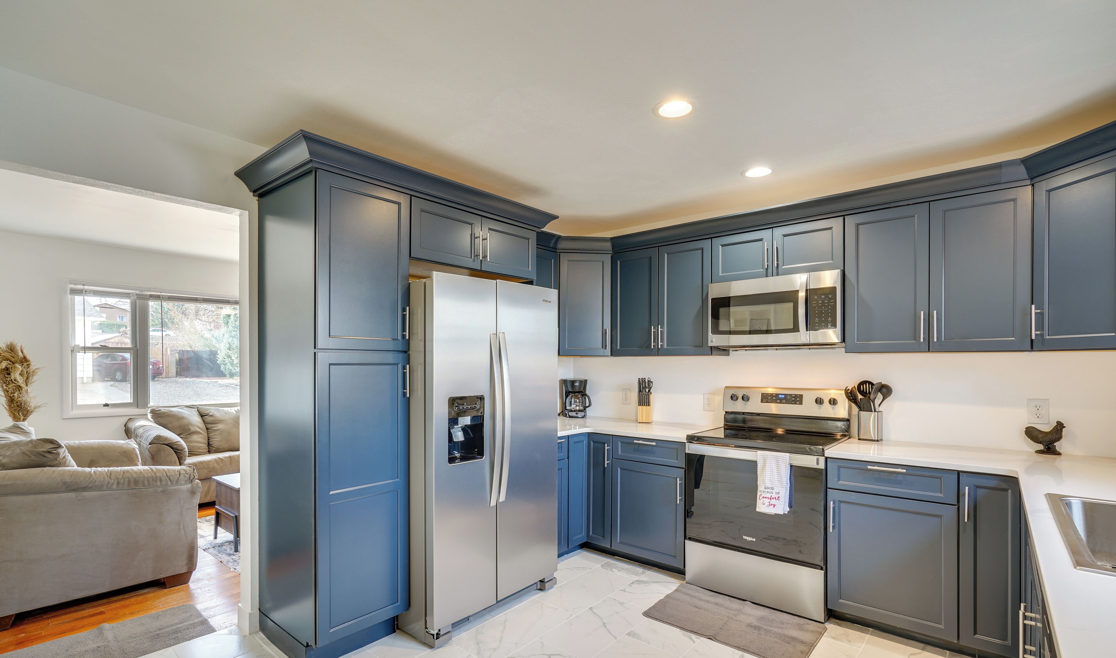 A modern kitchen with dark blue cabinets, stainless steel appliances, and a marble floor.