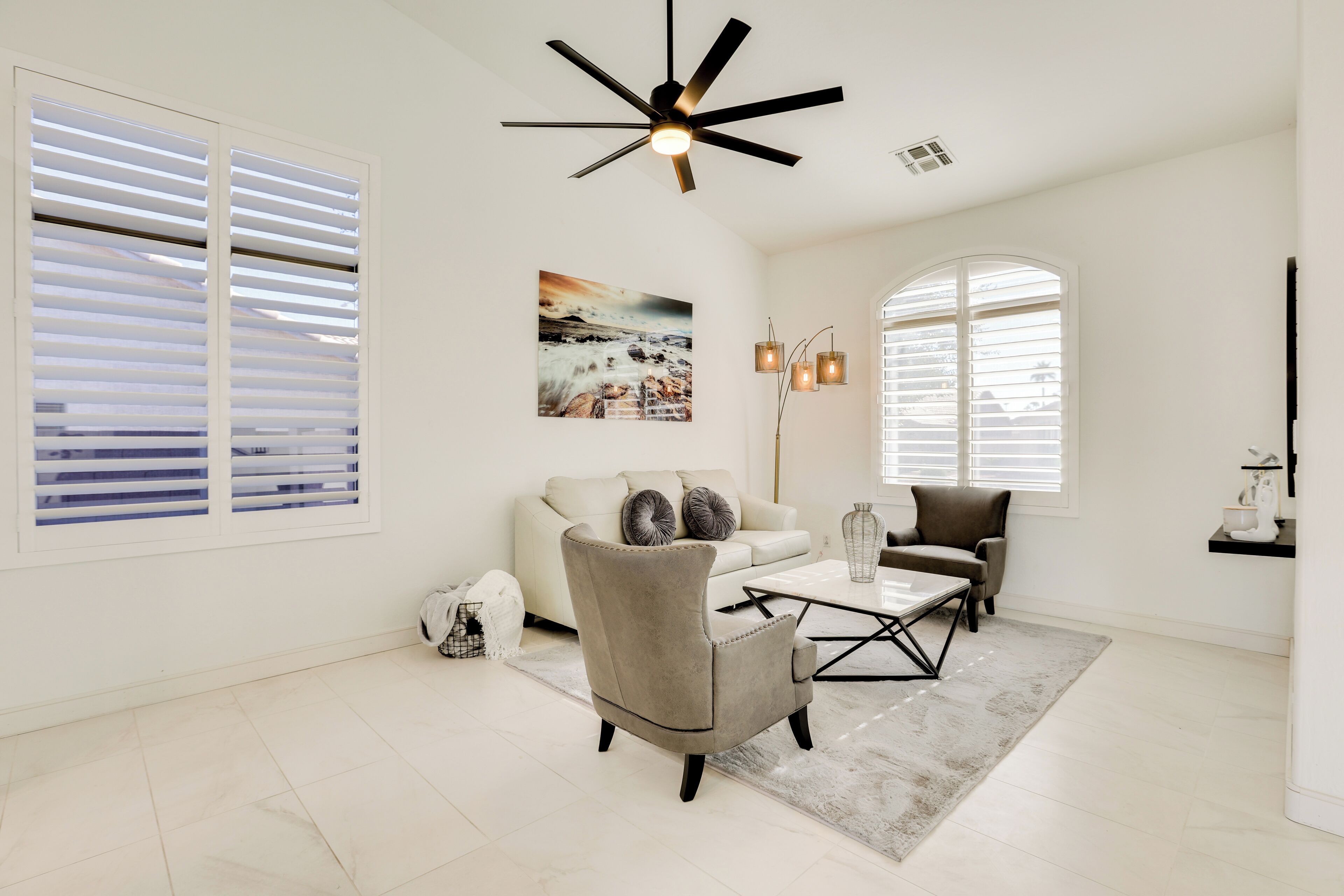 A spacious living room with a modern ceiling fan, a white sofa, a grey armchair, and a coffee table.