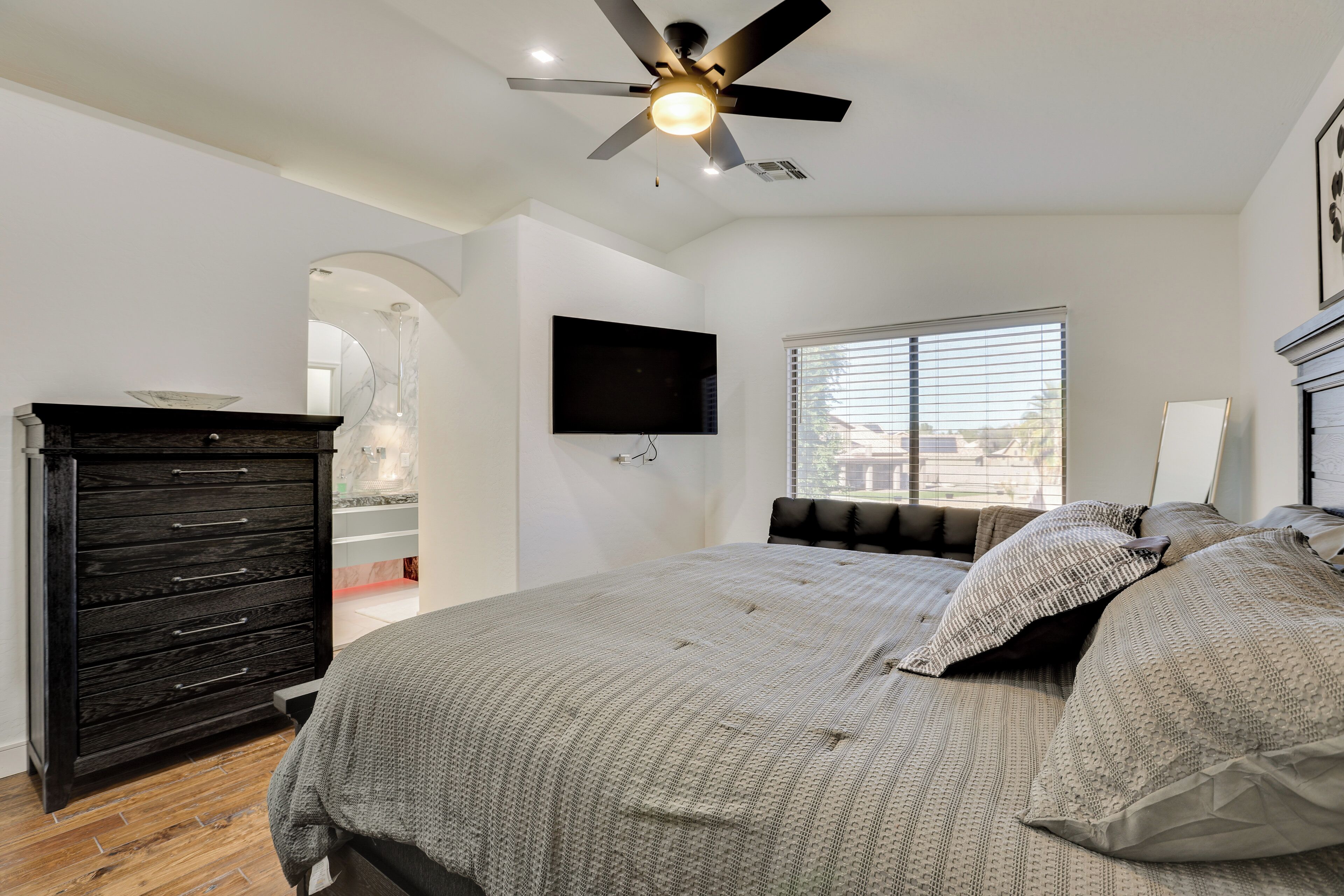 Une chambre à coucher comprenant un lit, une commode, un ventilateur de plafond, un téléviseur et une fenêtre.