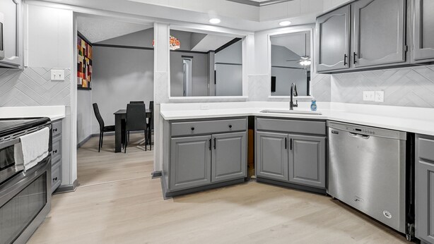 A modern kitchen with grey cabinets, a white countertop, and a dishwasher. There is a dining area with a black table and chairs in the background. - New Listing/NASA/ 4br 2ba 2000sq Sleeps10, Pet Friendly,Monthly discounts (League City)