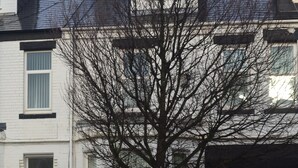 A residential street with two parked cars, a tree, and a white building with a black roof. - Ocean Road Rooms (South Shields)