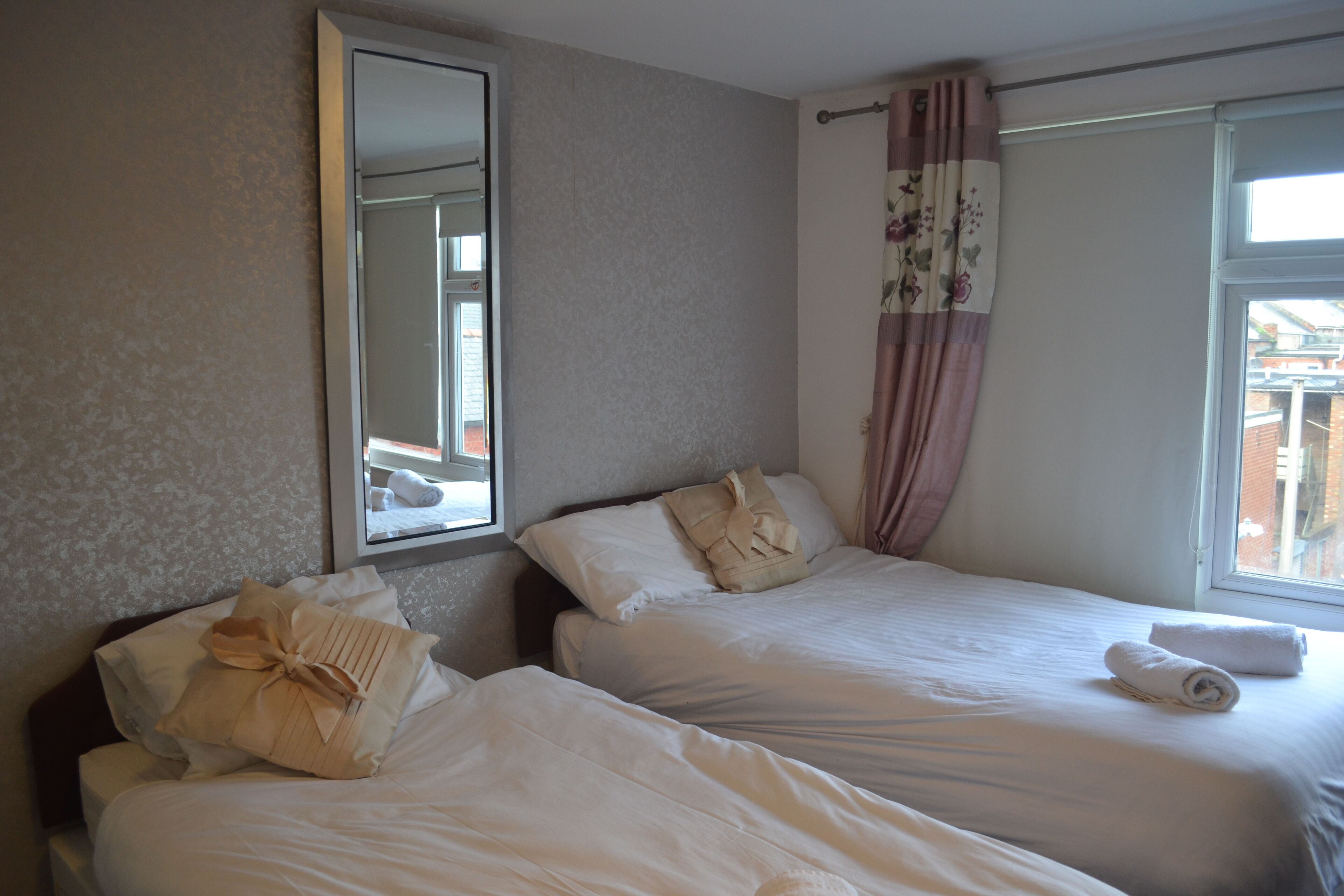 A hotel room with two beds, a large mirror, and a window with curtains.