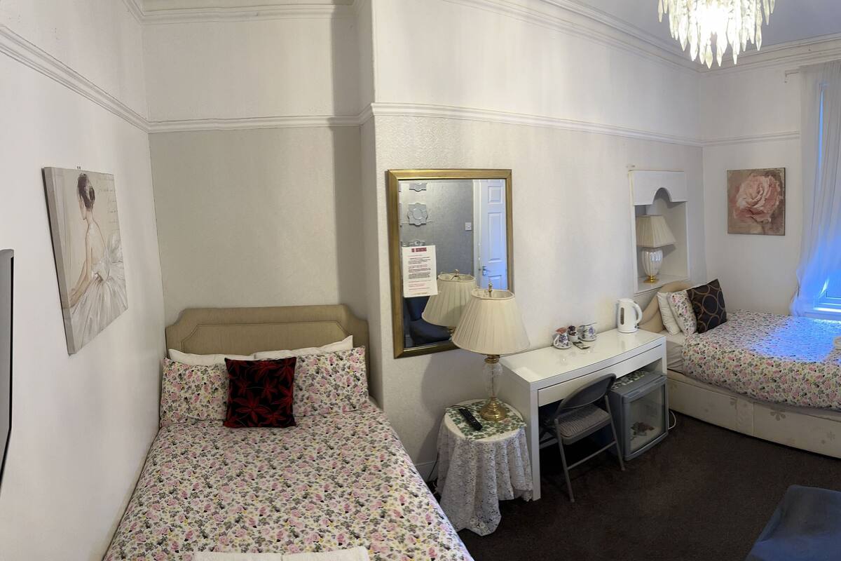 A hotel room with two single beds, a desk with a lamp, a mirror, and a small table.
