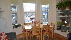 A dining area with a table and chairs, large windows, and a plant shelf. - Ocean Road Rooms (South Shields)