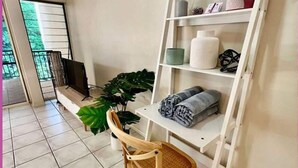Een badkamer met een houten stoel, een plank met handdoeken, een potplant en een raam met uitzicht op groen.