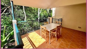 Een balkon met een tafel en stoelen, omgeven door een metalen hekwerk en uitzicht op groen.