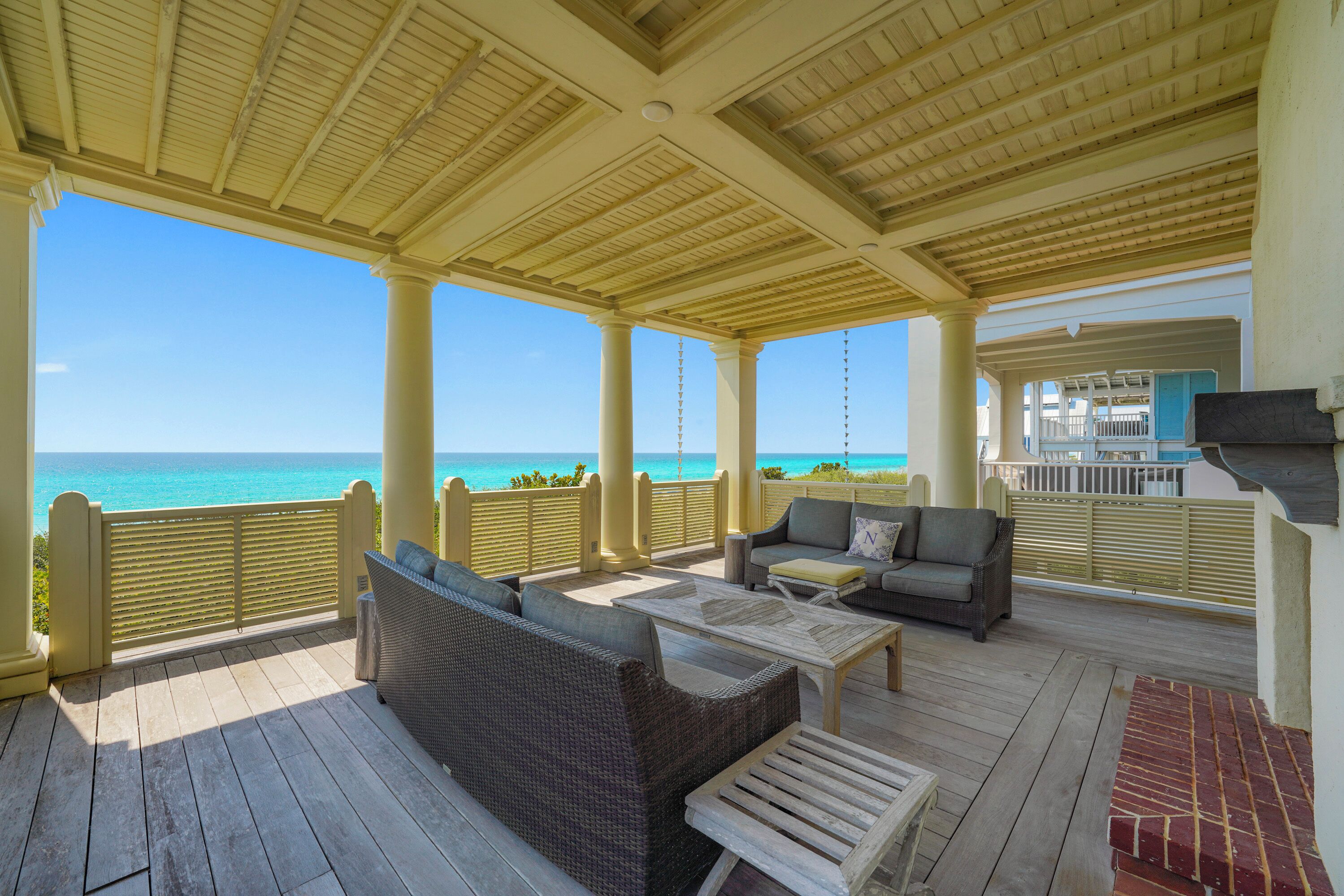 A covered outdoor area with a view of the ocean, furnished with wicker sofas and a coffee table.
