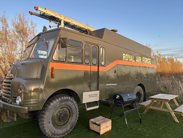 A vintage military-style vehicle labeled "ROYAL AIR FORCE" parked on grass with a picnic table and grill nearby.