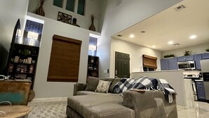 Un'ampia zona giorno con un'ampia sezione angolare, un tavolo da pranzo con sedie, una ventola a soffitto e un angolo cottura con elettrodomestici moderni.