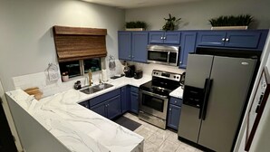 Una cucina moderna con mobili blu, un'isola in marmo, elettrodomestici in acciaio inossidabile e soffitto in legno.