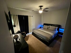A bedroom with a bed, a desk, a chair, a ceiling fan, and curtains.