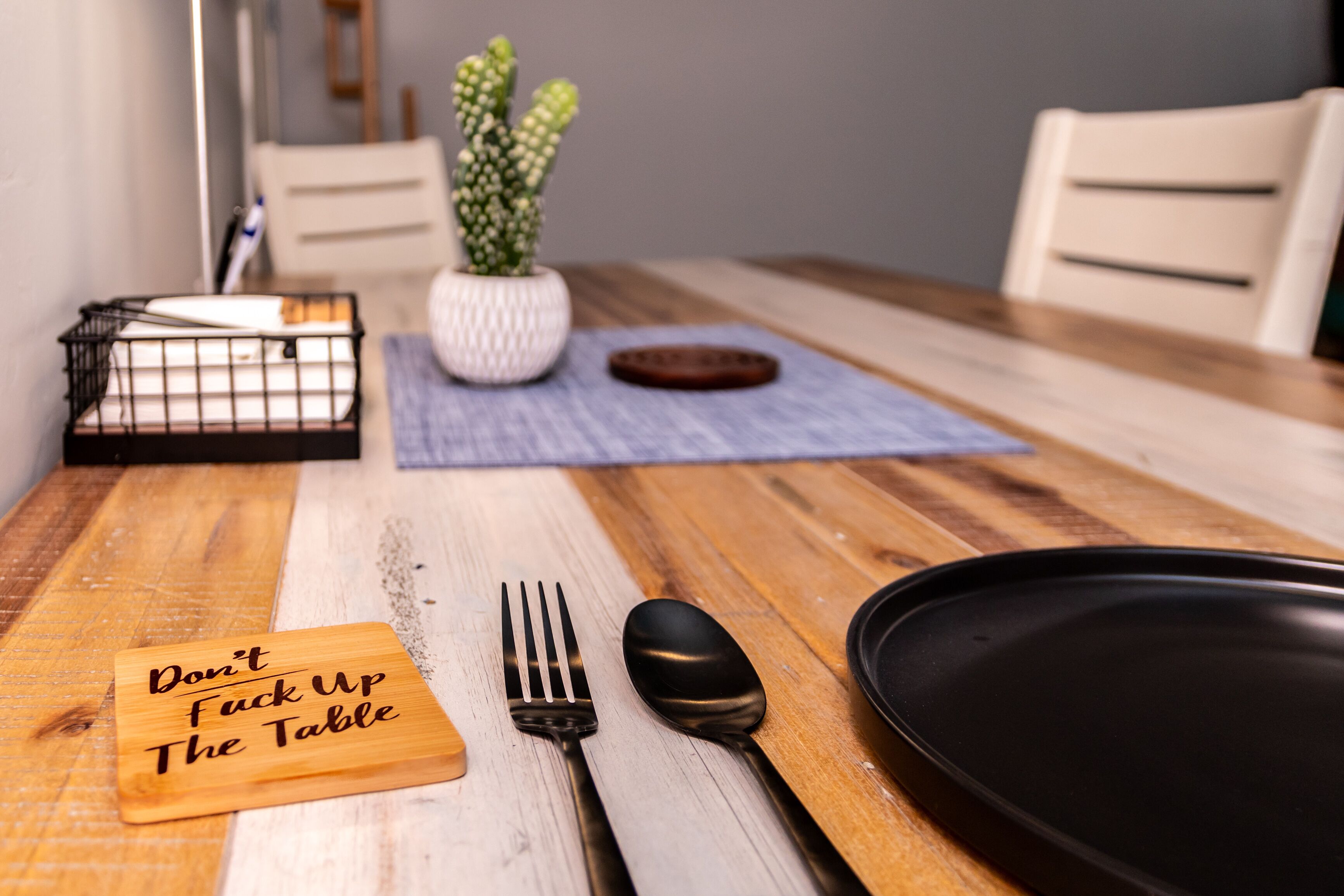 Une table à manger avec un set de table, une assiette noire, une cuillère, une fourchette et un panneau sur lequel on peut lire : « Ne salissez pas la table ».