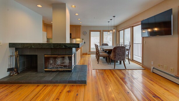 A modern kitchen with a built-in fireplace, wooden flooring, and a dining area with a large table and chairs. - The Great Scott Lodge (Snowbird)