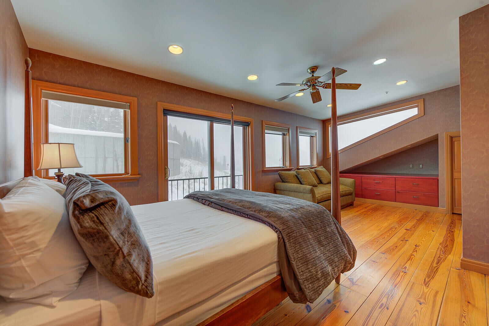 Een slaapkamer met een groot bed, een bureau, een stoel en uitzicht op een besneeuwd landschap door de ramen.