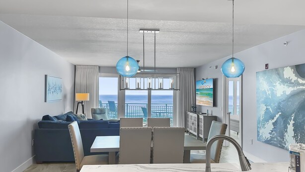 A modern hotel room with a dining area, a sofa, a large window with a view of the sea, and a kitchen with a marble countertop. - Luxury Beachfront Bliss – Blu’s Only 2BR Condo! (Fort Walton Beach)