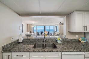 A kitchen with granite countertops, a stainless steel sink, and a view of a balcony with a dining area and ocean view. - FREE Beach Service, Golf &Perks! Long Beach Tower 3-303, Hot Tub, Gym & Pools (Panama City Beach)