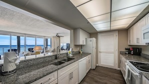 A modern kitchen with granite countertops, white cabinetry, a built-in oven, and a view of the ocean through large windows. - FREE Beach Service, Golf &Perks! Long Beach Tower 3-303, Hot Tub, Gym & Pools (Panama City Beach)