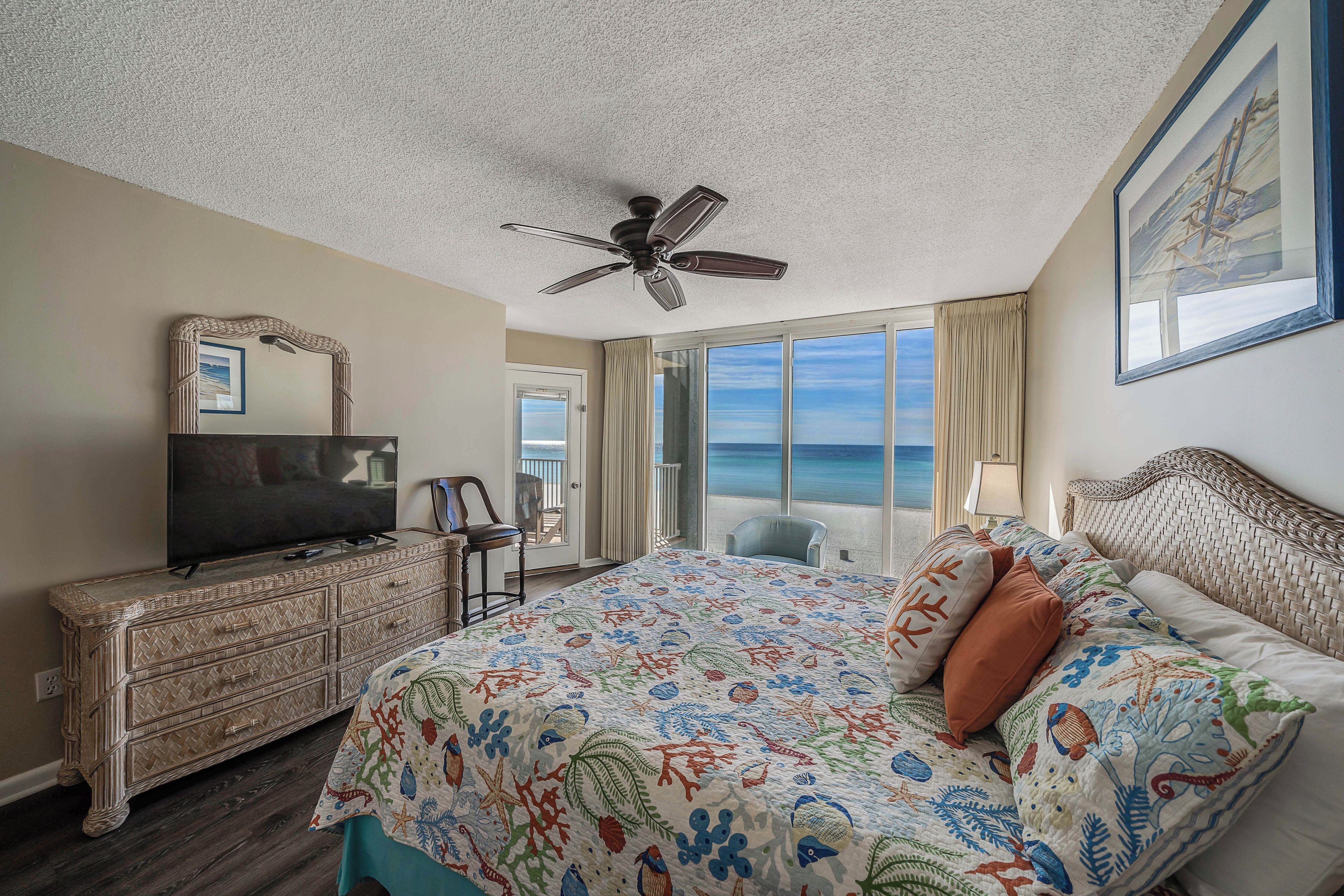 Ein Hotelzimmer mit einem großen Bett, einem Fernseher, einem Deckenventilator und Blick aufs Meer.