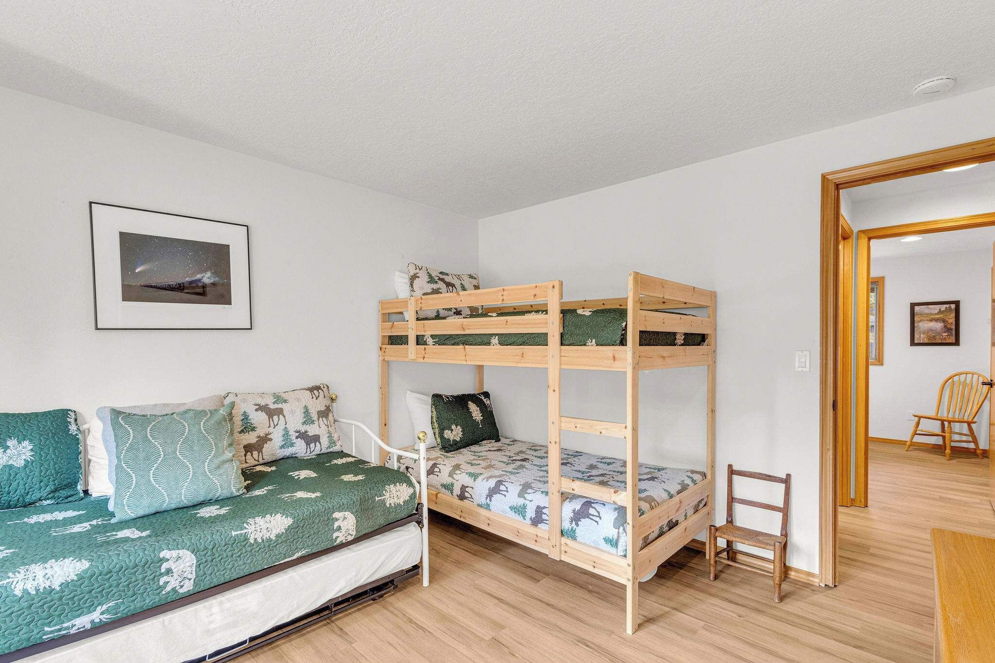Un lit superposé avec un lit inférieur et un canapé-lit, tous deux dotés de draps à motifs. Une petite chaise en bois se trouve à côté du lit superposé.