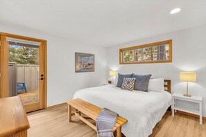 A bedroom with a bed, bedside tables, a bench, a door, and a window.