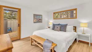 Un dormitorio con cama, mesitas de noche, un banco, una puerta y una ventana.