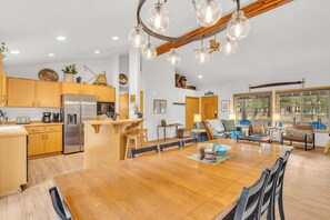 A modern kitchen with wooden cabinets, a stainless steel refrigerator, and a dining area with a wooden table and chairs.