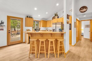A modern kitchen with wooden cabinets, a central island with stools, and a large window.