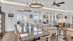 A spacious living room with a large wooden dining table, a sofa, and a ceiling fan. - Pineapple Beach (Islamorada)