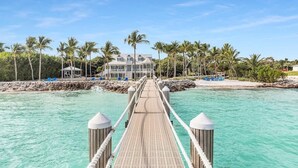 A wooden pier leading to a large house with a pool and palm trees. - Pineapple Beach (Islamorada)