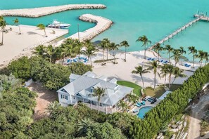 Une propriété située en bord de mer, comprenant une grande maison, une piscine et une jetée s’avançant dans des eaux turquoise.