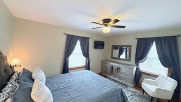 Une chambre à coucher comprenant un lit, une commode, une chaise, un ventilateur de plafond et un téléviseur.