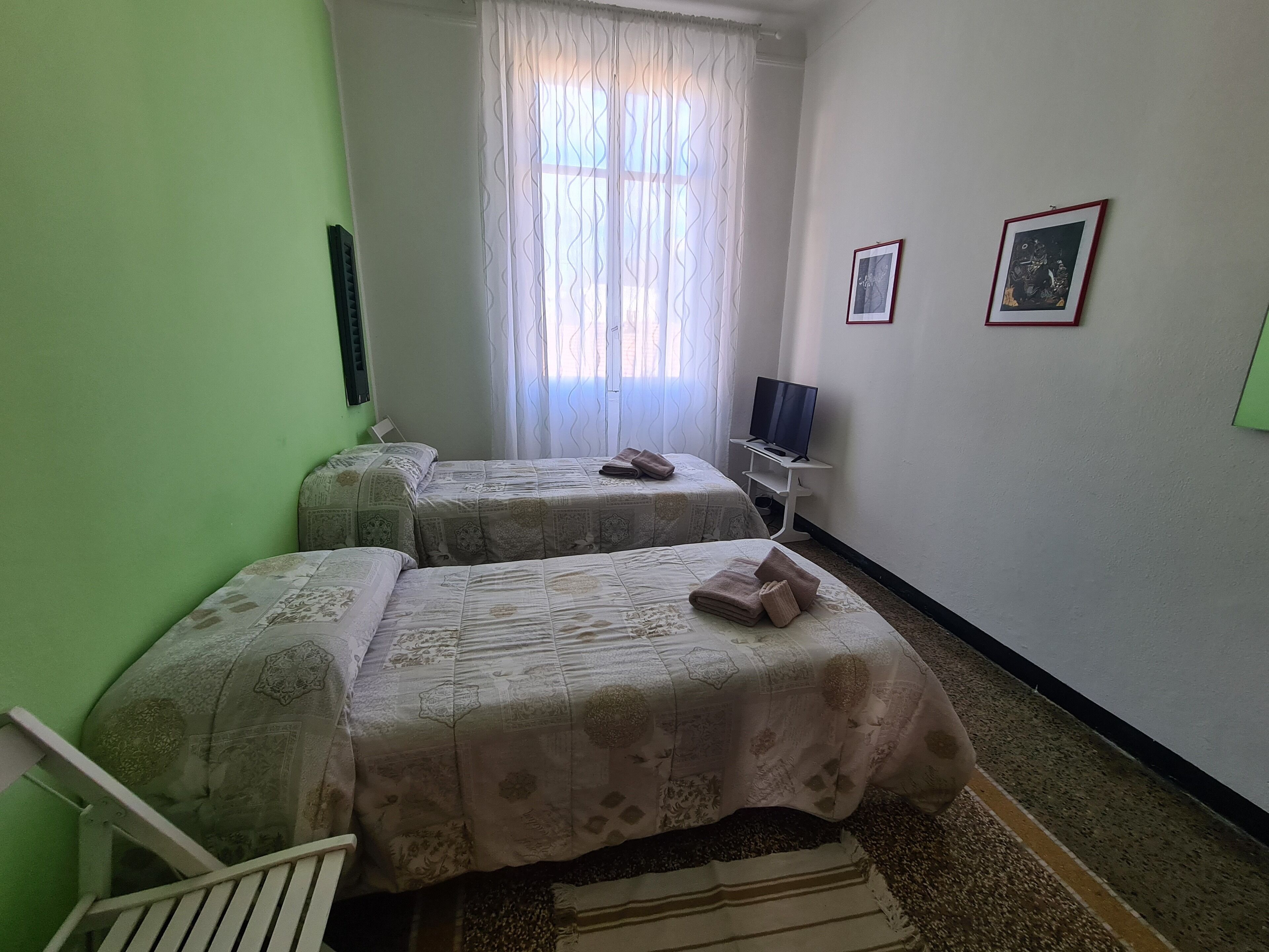 A room with two beds, a TV, and two framed pictures on the wall.