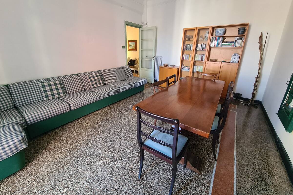 Ein Wohnzimmer mit einem grünen Sofa, einem Holzespeisetisch und einem Bücherregal.