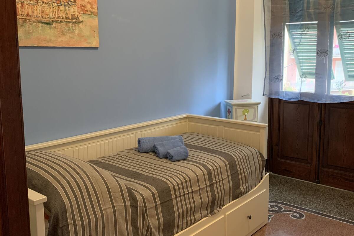 Ein Schlafzimmer mit Bett, Nachttisch, einem Wandbild und einem Fenster mit Vorhängen.
