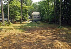 A house surrounded by a wooded area with a lawn and outdoor seating.