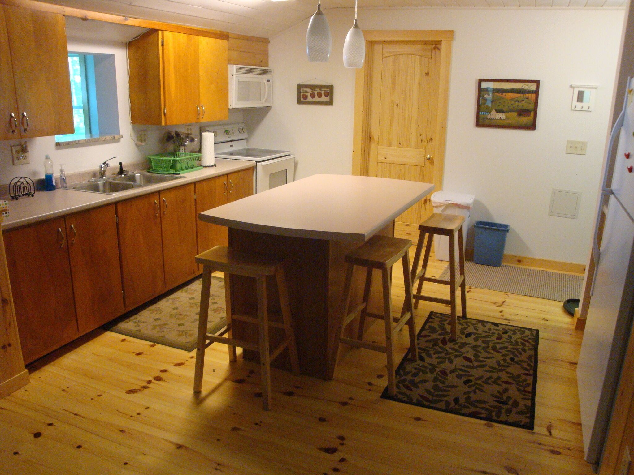 A kitchen with wooden cabinets, a white countertop, a central island with stools, a microwave, and a refrigerator.