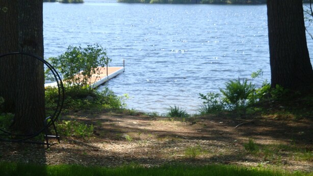 A lake with a dock extending into the water, surrounded by trees. - Charming cottage with stunning views and 180' of waterfront on Little Sebago. (Gray)