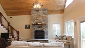 A cozy living room with a stone fireplace, wooden ceiling, and a sofa. - Stunning modern home in peaceful, private setting on desirable Long Lake. (Bridgton)