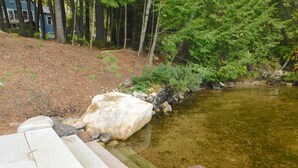 A stone pathway leading to a clear pond surrounded by trees and rocks. - Stunning modern home in peaceful, private setting on desirable Long Lake. (Bridgton)
