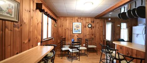 Una habitación con paneles de madera, una mesa de comedor y sillas, un reloj y una zona de cocina con ollas colgando sobre la encimera.