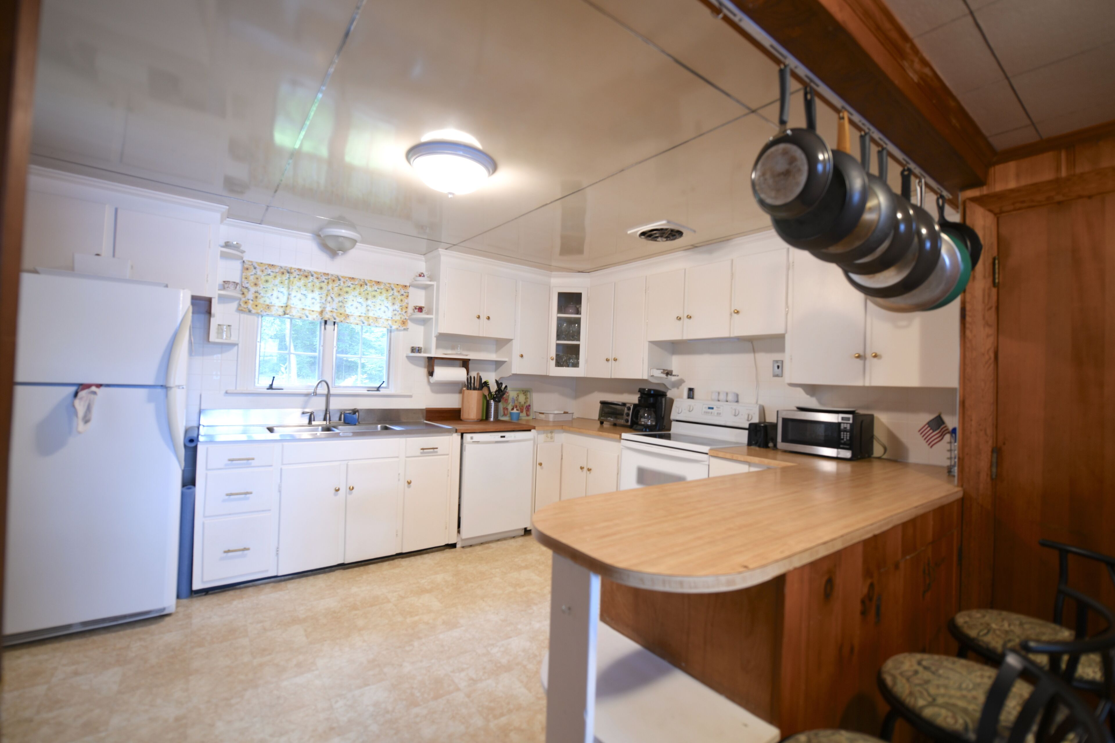A kitchen with white cabinets, a wooden countertop, and a hanging pot rack.
