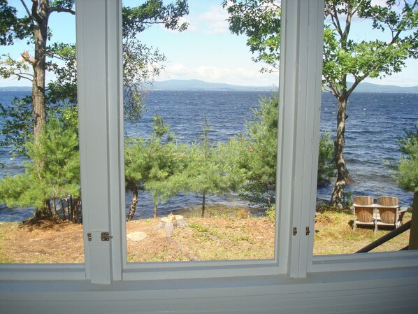 A view from a window overlooking a lake with trees and a wooden bench.