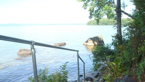 Eine Holztreppe führt zu einem felsigen Ufer an einem See, mit Metallgeländern und Blick auf das Wasser.