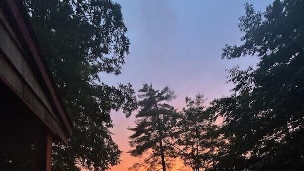 Une terrasse en bois offrant une vue sur un lac et des arbres au coucher du soleil.