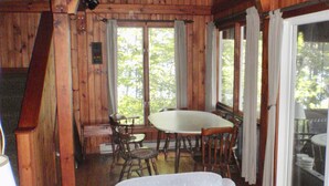 Une cabane en bois dotée d’un coin repas avec une table ronde et des chaises, de grandes fenêtres et une vue sur les arbres.