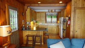 Une cuisine compacte avec des meubles en bois, un évier, une cuisinière et un réfrigérateur. On y trouve également un petit coin salon avec un canapé bleu et un tapis vert.
