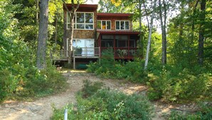 Une cabane dotée d’une terrasse et d’un quai s’avançant dans une étendue d’eau, le tout entouré d’une forêt dense.