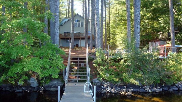 Une jetée en bois menant à une maison entourée d’arbres.