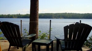 Une terrasse avec deux fauteuils Adirondack et une petite table, donnant sur un lac paisible dont les rives sont bordées d’une forêt.