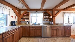 Une cuisine dotée de meubles en bois, de plans de travail en granit, d’un lave-vaisselle en acier inoxydable et d’étagères intégrées pour ranger les ustensiles de cuisine.